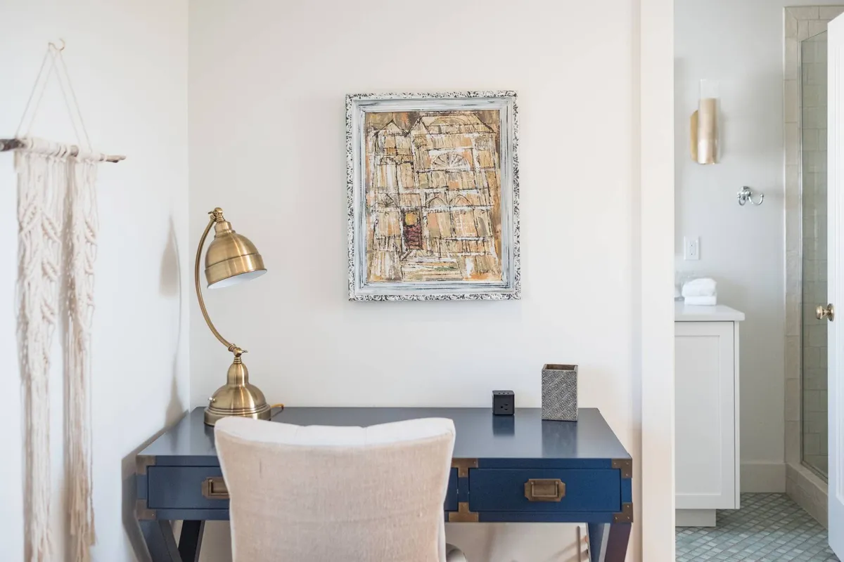 A serene workspace setting with a sleek desk, chair, lamp, and artwork on the wall. The arrangement balances productivity and creativity, providing a quiet spot for remote work, planning adventures, or enjoying a reflective moment.