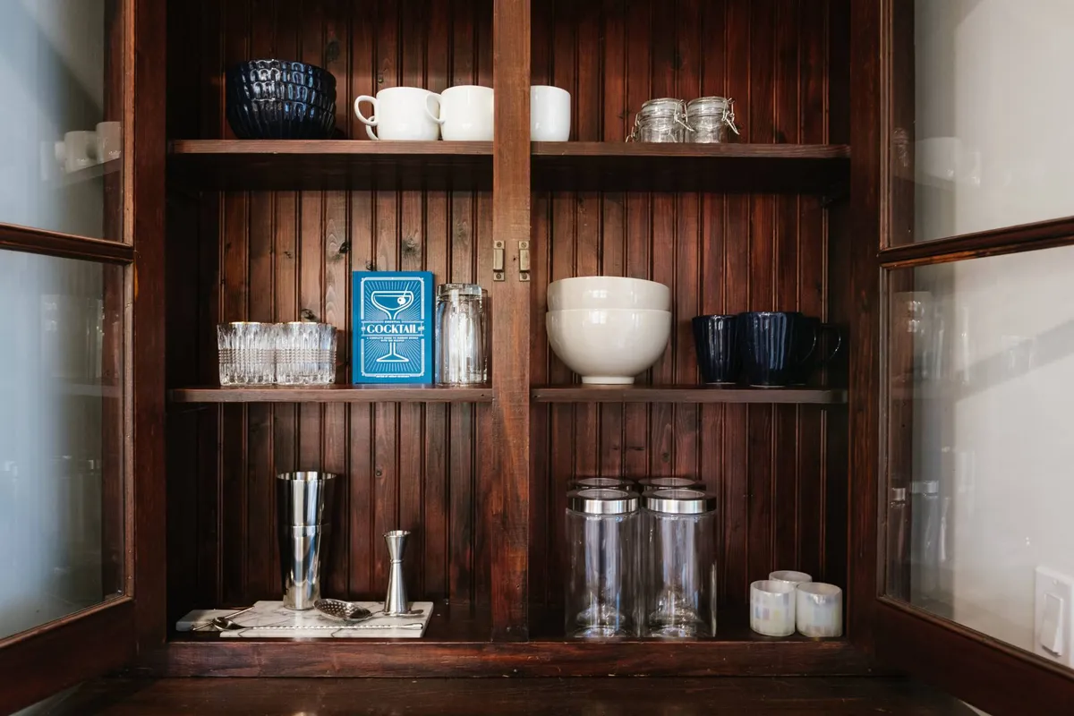 The image shows stylish wooden shelving filled with cocktail recipe books, glassware, and ceramic bowls. The space is set up for entertaining guests, with an inviting and functional atmosphere that hints at social gatherings and relaxed evenings.