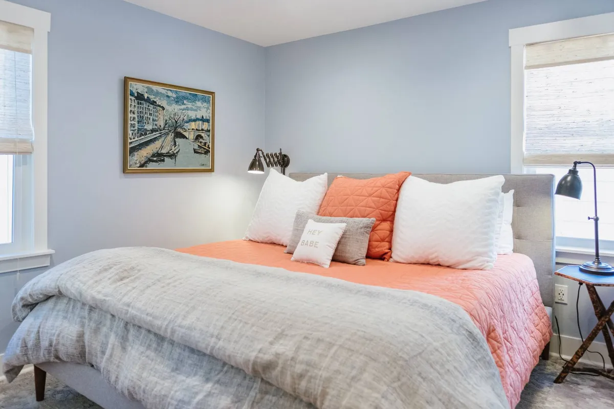 A comfortable bedroom scene featuring a well-made bed, soft lighting from a lamp, and artwork above the headboard. The mood is intimate and cozy, perfect for relaxing, reading, or enjoying a quiet coffee in bed.