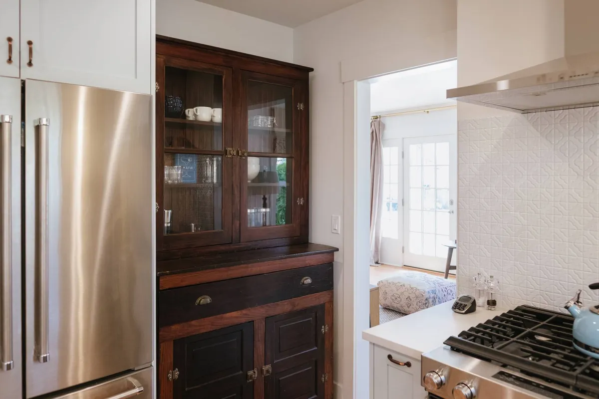 A kitchen scene centering on a stainless steel refrigerator, wooden cabinetry, and a spacious countertop, with an open doorway leading into another room. The atmosphere feels warm and welcoming, showcasing thoughtful design and functional space for entertaining and culinary gatherings.