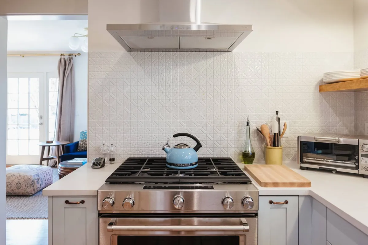 This image captures a warm, welcoming kitchen space with a stainless steel stove, blue kettle, and wooden cutting board. The setting suggests a functional hub for cooking and gathering, with subtle cues of shared culinary experiences.
