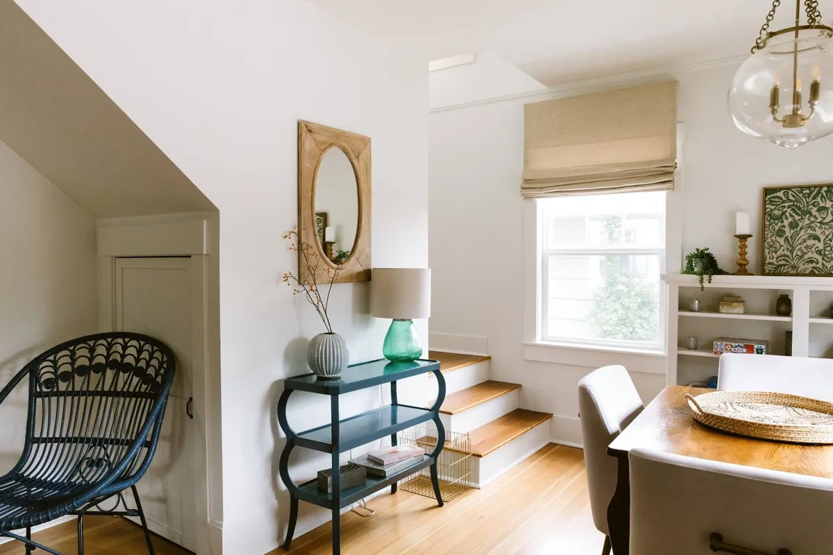 A cozy, welcoming dining area with a blue chair, decorative mirror, green vase, and a wooden dining table, highlighted by soft natural light. The setting is perfect for sharing meals or relaxing with friends after a day of exploring local wineries.